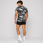 A man is shown from behind wearing a gray and black camouflage t-shirt, black athletic shorts, white Nike socks, and white Nike running shoes against a light gray studio background.