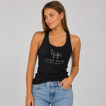 A woman modeling a black racerback tank top with a white 'Luxe Hair' logo printed on the chest, paired with light blue jeans, against a solid light gray background.