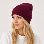 A woman with blonde hair wearing a ribbed knit beanie in deep burgundy, photographed against a clean off-white background.