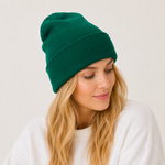 A woman with blonde hair wearing a dark green ribbed knit beanie and a white sweatshirt, photographed against a plain light background.