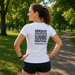 A woman standing outdoors on a park path wearing a white short-sleeve T-shirt with black text reading 'KIRKCALDY PARKS RUNNING FESTIVAL' and a website URL on the back, paired with black shorts.