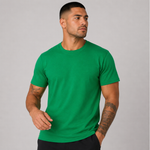 A man wearing a solid green crew-neck t-shirt, shown from the waist up against a neutral gray studio background.