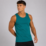 A muscular man wearing a teal green sleeveless tank top and black athletic shorts, posing against a solid light gray studio background.
