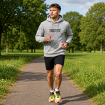 A man jogging on a paved path in a park, wearing a heather Gray hoodie with a colourful graphic print that reads 'RUNNING FEEL GOOD' and black running shorts.