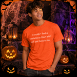 A smiling young man wearing an orange graphic t-shirt with white text that reads 'I couldn't find a costume so this t-shirt will just have to do.' He is posed in a Halloween-themed setting with jack-o'-lanterns, cobwebs, and lanterns.