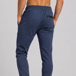 A close-up back view of a person wearing heathered navy blue jogger sweatpants with an elastic waistband, side pockets, and a small black zippered pocket on the back.