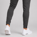 Close-up of a person's legs wearing dark grey heather jogger pants and white sneakers, shown from the back against a light grey studio background.