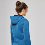 A woman shown from the back wearing a heathered blue hooded sweatshirt with a black inner collar, set against a plain light grey studio background.