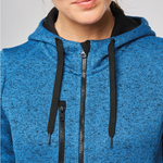 Close-up of a person wearing a heathered blue zip-up hoodie with black drawstrings and a black inner hood lining, cropped from the lower face to the upper torso against a light grey background.