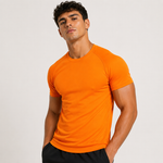 A man wearing a bright orange short-sleeve athletic t-shirt with raglan sleeves, paired with black shorts, photographed against a light gray studio background.