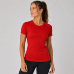 A woman wearing a bright red short-sleeve athletic crewneck t-shirt and black leggings, standing against a light grey studio background.