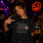A woman at a nightclub wearing a black graphic t-shirt that reads 'Pretend I have a gyatt' with a peach graphic. She is pointing at the text on her shirt and holding a black 'BOO' cup.