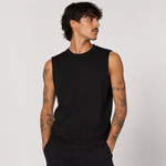 A man with dark hair and tattoos wearing a black sleeveless crewneck tank top, photographed against a light gray studio background.