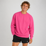A smiling young man wearing a bright pink crewneck sweatshirt and black athletic shorts with a small white Nike swoosh, standing against a light gray studio background.
