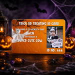 A Halloween-themed custom ID card displayed on a dark wooden surface surrounded by spooky props including jack-o'-lanterns, cobwebs, a spider, candy, and bats. The card is orange with white text reading 'TRICK OR TREATING ID CARD' and includes a photo placeholder of a child in a cow costume holding a sign.