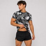 A muscular man wearing a gray and black camouflage t-shirt and black athletic shorts, posing against a light gray studio background.