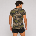 A man shown from the back wearing a short-sleeve crewneck t-shirt with an olive green, brown, and black camouflage pattern, paired with black athletic shorts, against a light gray studio background.