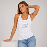 A woman modeling a white racerback tank top with a colorful 'LH' logo and 'LUXE HAIR HAIR DESIGN' text on the front, paired with light blue jeans against a light gray studio background.
