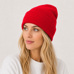 A woman with blonde hair wearing a bright red ribbed knit beanie hat, photographed against a light gray studio background.