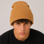 A close-up of a man wearing a ribbed knit beanie in camel brown, paired with a black crewneck shirt against a light grey background.