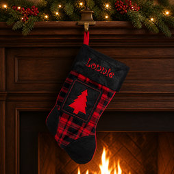 A personalized Christmas stocking with a red and black plaid pattern, a black faux fur cuff embroidered with the name 'Lonnie' in red, and a red tree applique, hanging from a fireplace mantel decorated with pine garlands and lights.