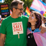 A smiling man and woman at a pride parade. The man wears a bright green T-shirt with a sign that reads 'THIS IS A SAFE SPACE' and a small rainbow heart.