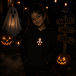 A young girl wearing a black hoodie with a glowing orange skeleton graphic on the chest, standing in a spooky Halloween setting with jack-o'-lanterns, a ghost decoration, and a 'Beware Spooky' sign.