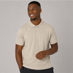 A man wearing a sand coloured short-sleeve polo shirt, standing against a solid grey studio background.