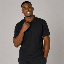 A smiling man wearing a black short-sleeve polo shirt, standing against a plain grey studio background.