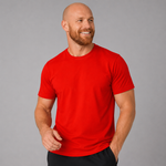 A smiling bald man with a beard wearing a bright red crew-neck t-shirt and black shorts, standing against a solid gray studio background.