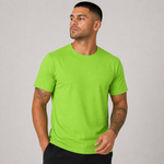 A man wearing a bright lime green crew-neck t-shirt and black pants, standing against a neutral gray studio background.