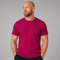 A man wearing a bright magenta short-sleeve crewneck t-shirt, standing against a solid gray studio background.