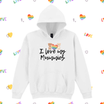 A white pullover hoodie with a front kangaroo pocket and a graphic print that reads 'I love my Mummies' in black script, featuring two teddy bears with a rainbow heart. The hoodie is displayed on a white background patterned with small rainbow hearts and the word 'LOVE'.