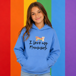 A young girl with long brown hair wearing a light blue hoodie with the text 'I love my Mummies' and a small cartoon bear graphic, standing in front of a vibrant rainbow-striped background.
