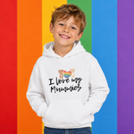 A young boy smiling and wearing a white hoodie with a graphic that reads 'I love my Mummies' with teddy bears and a rainbow heart. The background consists of vertical rainbow stripes in red, orange, yellow, green, blue, and purple.