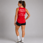 A woman is shown from the back wearing a bright red athletic tank top with white text that reads 'Glenrothes Triathlon Club' and 'Just Tri-Go'. She is also wearing black shorts, white socks, and gray running shoes against a solid gray studio background.