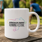A white ceramic mug with a colourful outline map graphic and the text 'KIRKCALDY PARKS RUNNING FESTIVAL' sits on a wooden table outdoors, with blurred people jogging in the background.