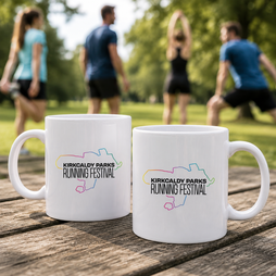 Two white ceramic mugs printed with the Kirkcaldy Parks Running Festival logo, placed on a wooden table with a blurred outdoor park scene in the background.