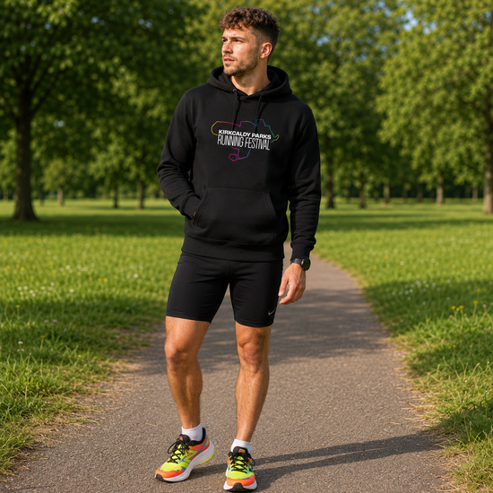 A man wearing a black hoodie and black running shorts stands on a paved path in a park, with green grass and trees in the background. The hoodie has a colourful graphic on the chest that reads 'Aberdeen Fairs Running Festival'.