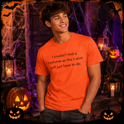 A smiling young man wearing an orange graphic t-shirt with the text 'I couldn't find a costume so this t-shirt will just have to do.' posed in a spooky Halloween-themed setting with pumpkins, cobwebs, and lanterns.