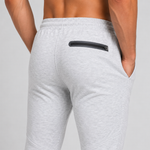 Close-up back view of a person wearing light heather grey jogger sweatpants with a side pocket and a black zipper detail, against a light grey studio background.