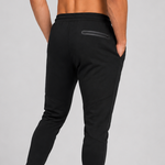 Black athletic jogger pants shown from the back on a model, featuring a zippered pocket on the upper thigh and ribbed ankle cuffs, paired with white sneakers against a light grey studio background.