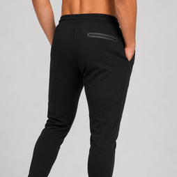 Black athletic jogger pants shown from the back on a model, featuring a zippered pocket on the upper thigh and ribbed ankle cuffs, paired with white sneakers against a light grey studio background.