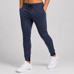A person wearing navy blue jogger sweatpants with a drawstring waist and elastic cuffs, paired with white sneakers, shown from the waist down against a light grey studio background.