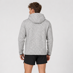 A man viewed from the back wearing a light grey heathered hooded sweatshirt and black athletic shorts against a plain light grey studio background.