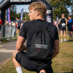 A man wearing a black drawstring backpack with a colourful 'Kirkcaldy Park's Running Festival' logo on the back, photographed from behind in an outdoor park setting.