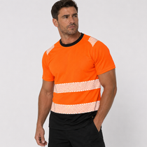 A man wearing a bright orange short-sleeve high-visibility work shirt with black trim and diagonal white reflective stripes, paired with black shorts, against a light gray studio background.