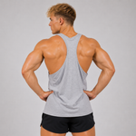 A muscular man shown from the back wearing a light gray racerback tank top and black athletic shorts, standing against a solid light gray studio background.