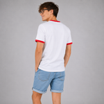 A man wearing a white ringer t-shirt with red trim on the collar and sleeve cuffs, paired with light blue denim shorts, photographed from the back against a solid gray studio background.