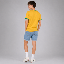 A man wearing a yellow ringer t-shirt with green trim, light blue denim shorts, white socks, and white sneakers, photographed from the back against a solid gray studio background.